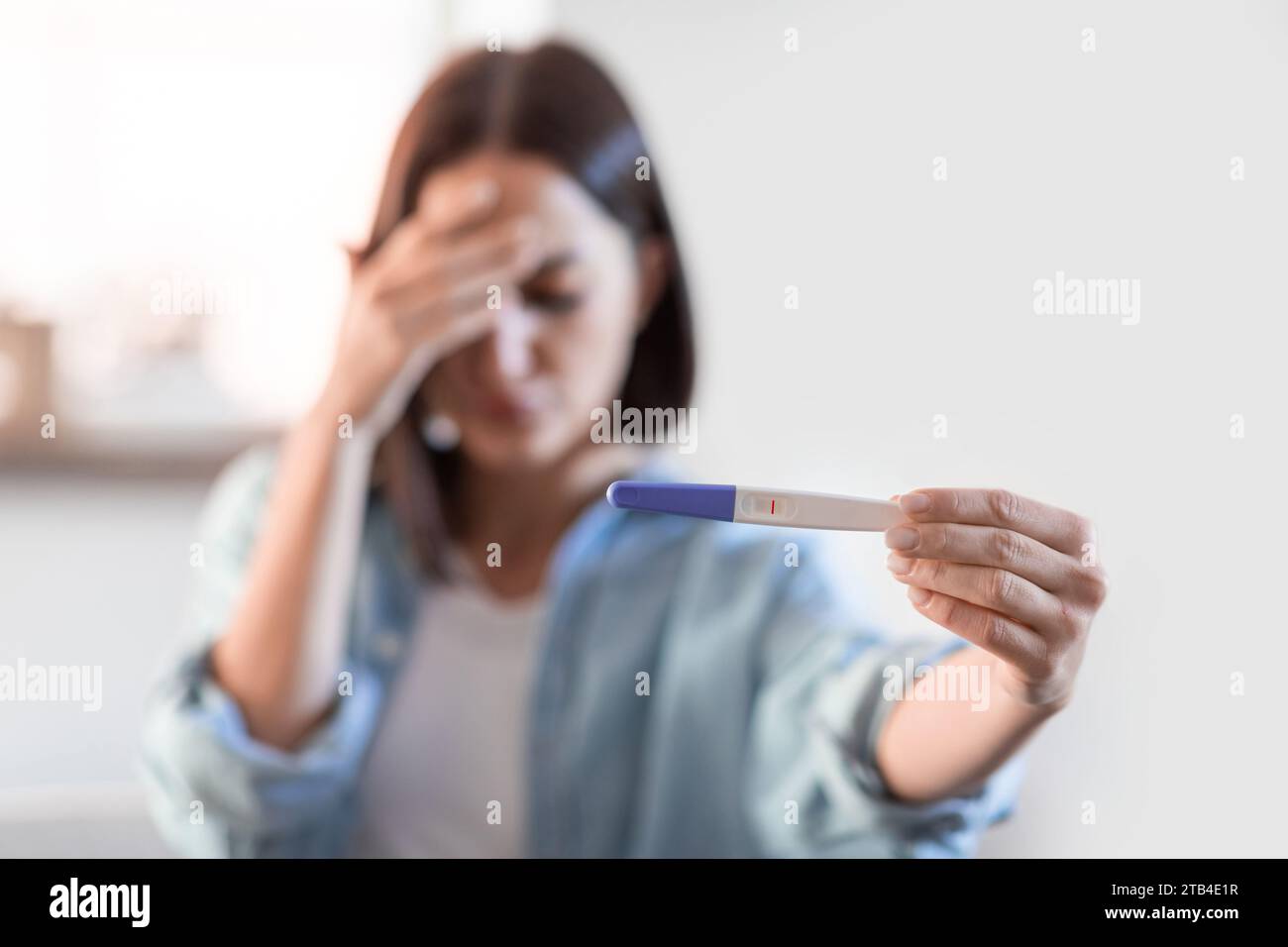 Deprimierte unerkennbare Dame mit negativem Schwangerschaftstest im häuslichen Innenraum Stockfoto
