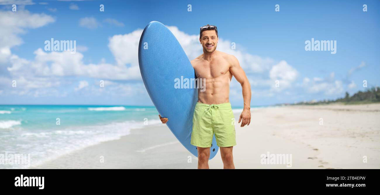 Mann am Strand, der ein Surfbrett hält und lächelt Stockfoto