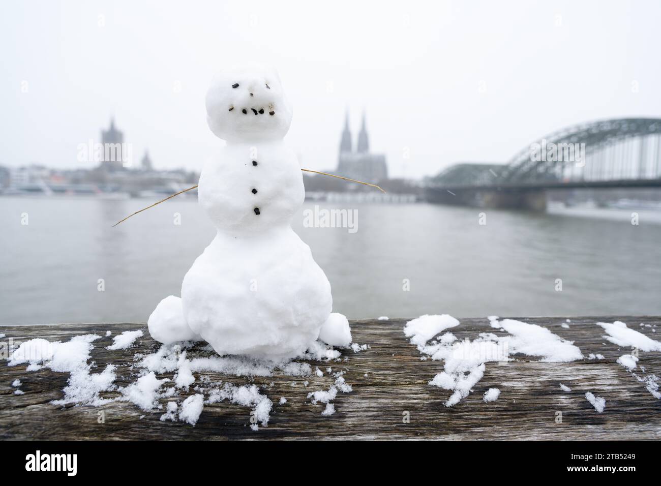 Ein kleiner Schneemann auf dem hölzernen Geländer des Rheinboulevards mit dem Dom im Hintergrund während eines seltenen Schneefalls Anfang dezember Stockfoto