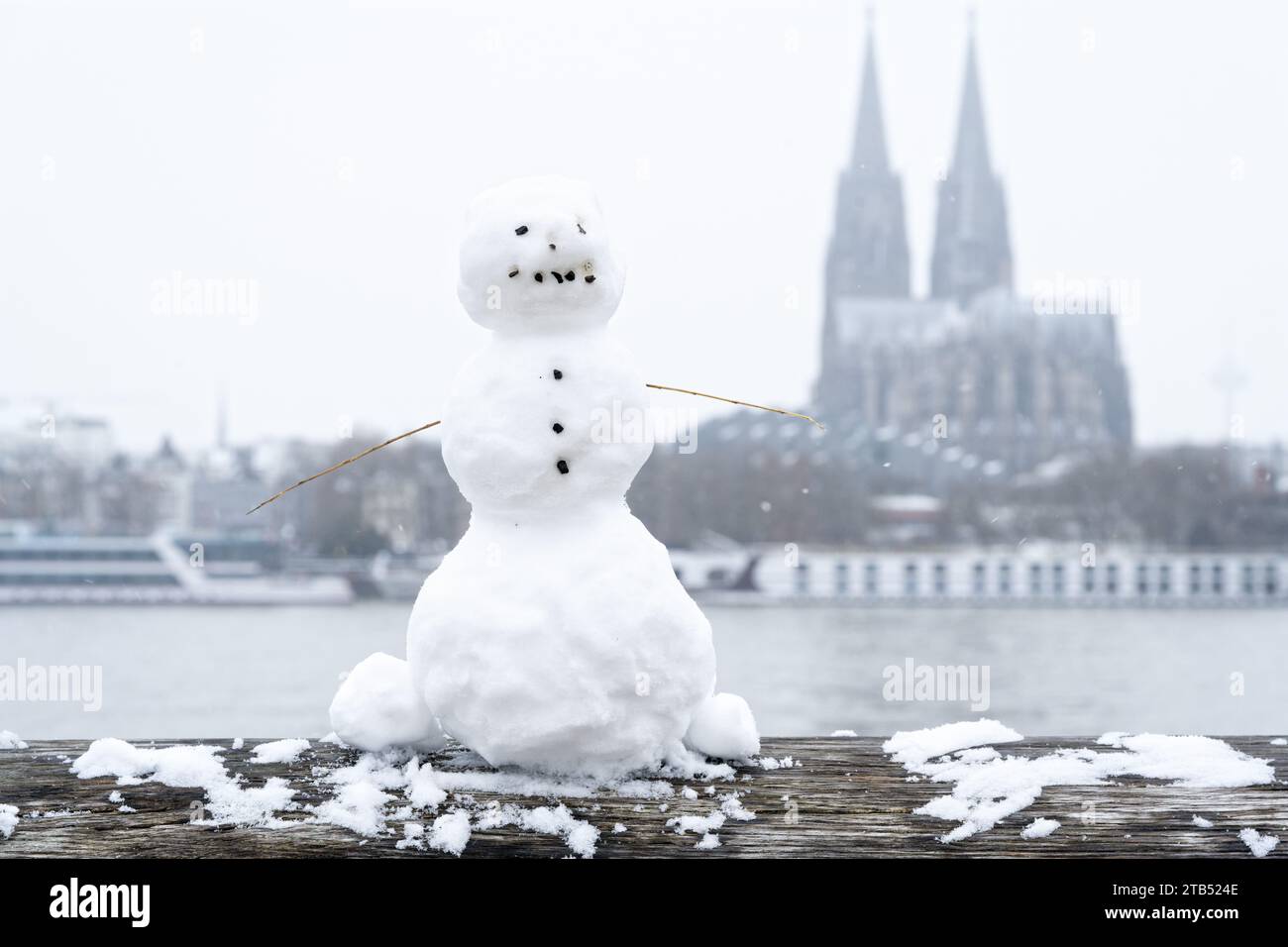 Ein kleiner Schneemann auf dem hölzernen Geländer des Rheinboulevards mit dem Dom im Hintergrund während eines seltenen Schneefalls Anfang dezember Stockfoto