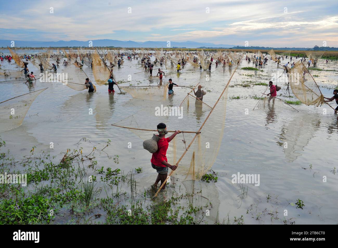 Ländliche Menschen, die mit Bambusfischfallen und -Netzen bewaffnet sind, nehmen an der Feier eines 200-jährigen Winterfischfestivals im Jofra Beel of gasbari union of Kanaighat upazila in Sylhet, Bangladesch, Teil. Stockfoto