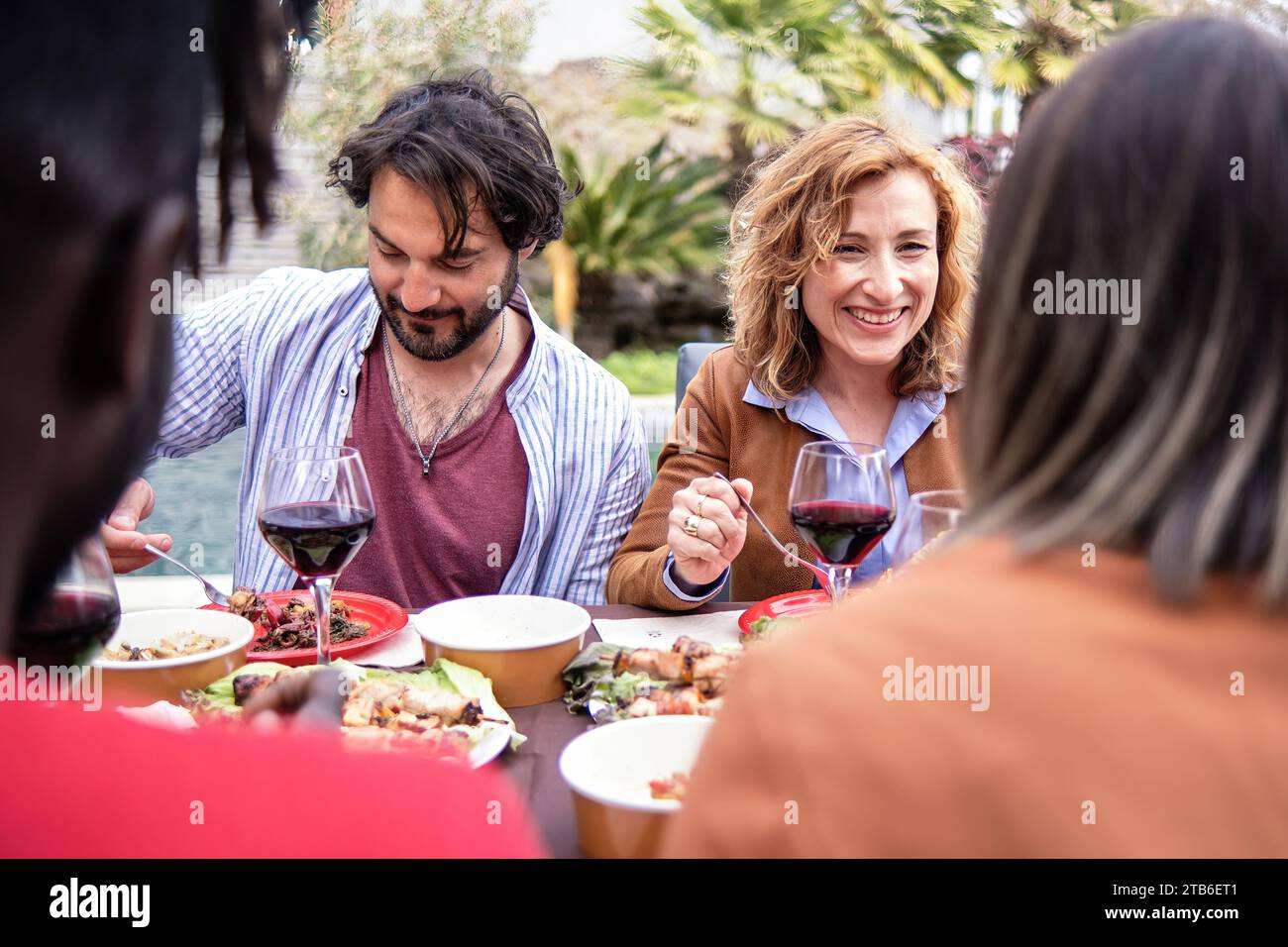 Eine Gruppe von Freunden teilt eine warme, intime Mahlzeit im Freien, genießt Wein und führt zu fröhlichen Gesprächen. Stockfoto