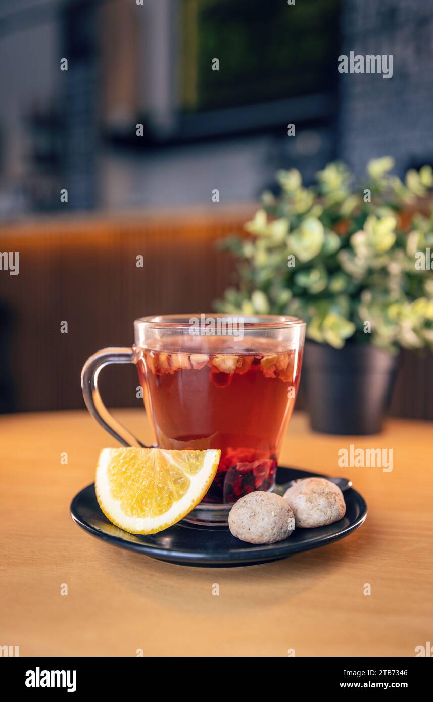 Heißer Früchtetee in einer transparenten Tasse serviert mit Zitronenscheibe und zwei Keksen Stockfoto