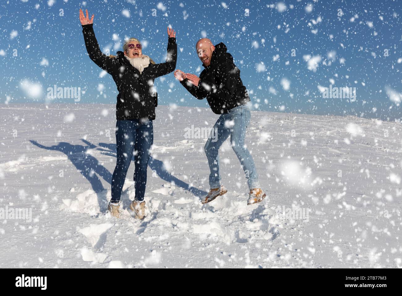 Ein junges Paar, bestehend aus einer Frau und einem Mann, springt in die Luft im Schnee und hat Spaß miteinander Stockfoto