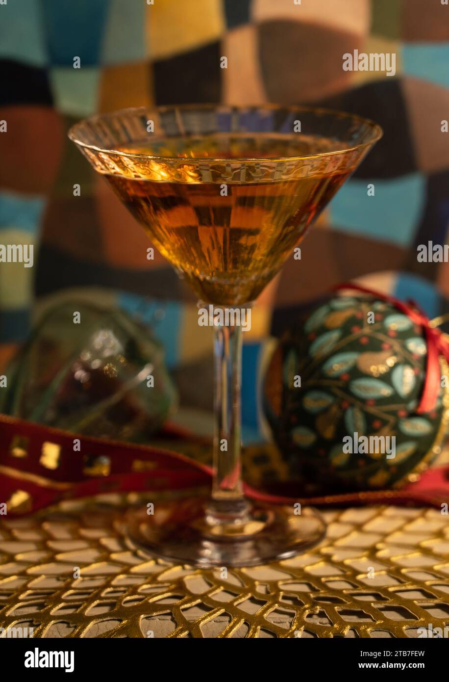 Klassischer Champagner-Cocktail in Martini-Glas mit Weihnachtsdekoration mit Kugeln und rotem Band auf einer goldenen Matte Stockfoto