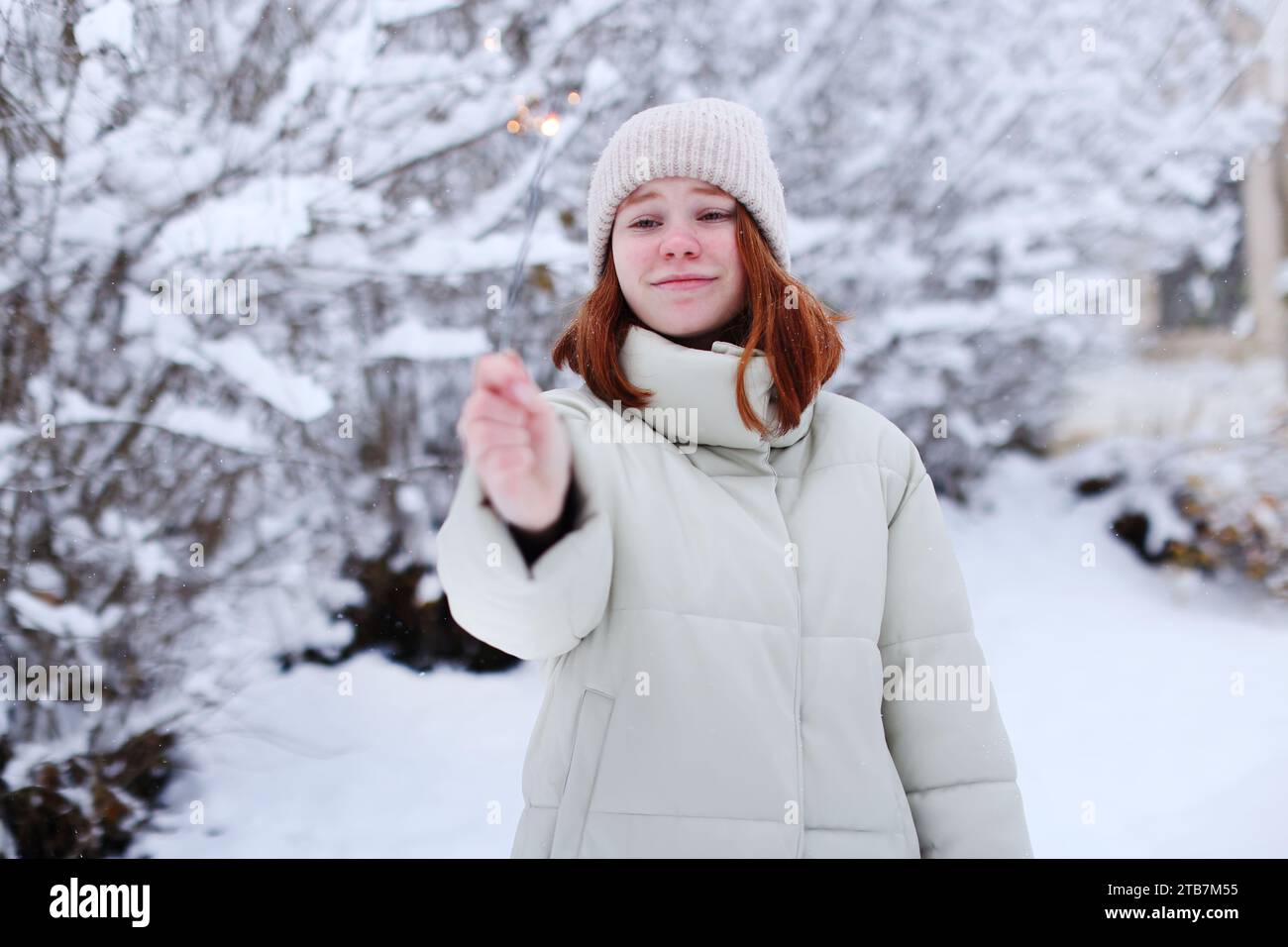 Fröhliche junge Frau, die im Winterwald einen Glitzer in der Hand hält. Weihnachten, Neujahr. Stockfoto