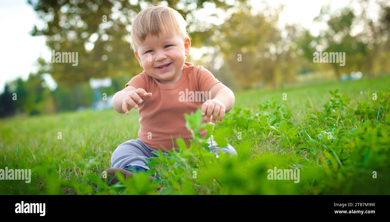 Niedliches lachendes Baby, das Spaß am Sonnenschein auf Gras hat. Sommerzeit, glückliches Baby Stockfoto