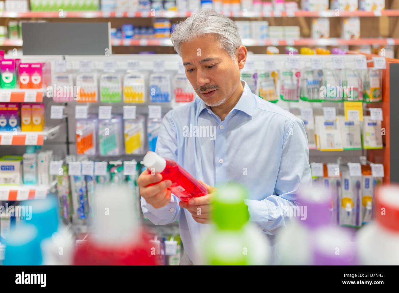 Leitender Mann, der rote Produkte hält und Informationen überprüft, während er in einem pharmazeutischen Geschäft am Regal steht Stockfoto