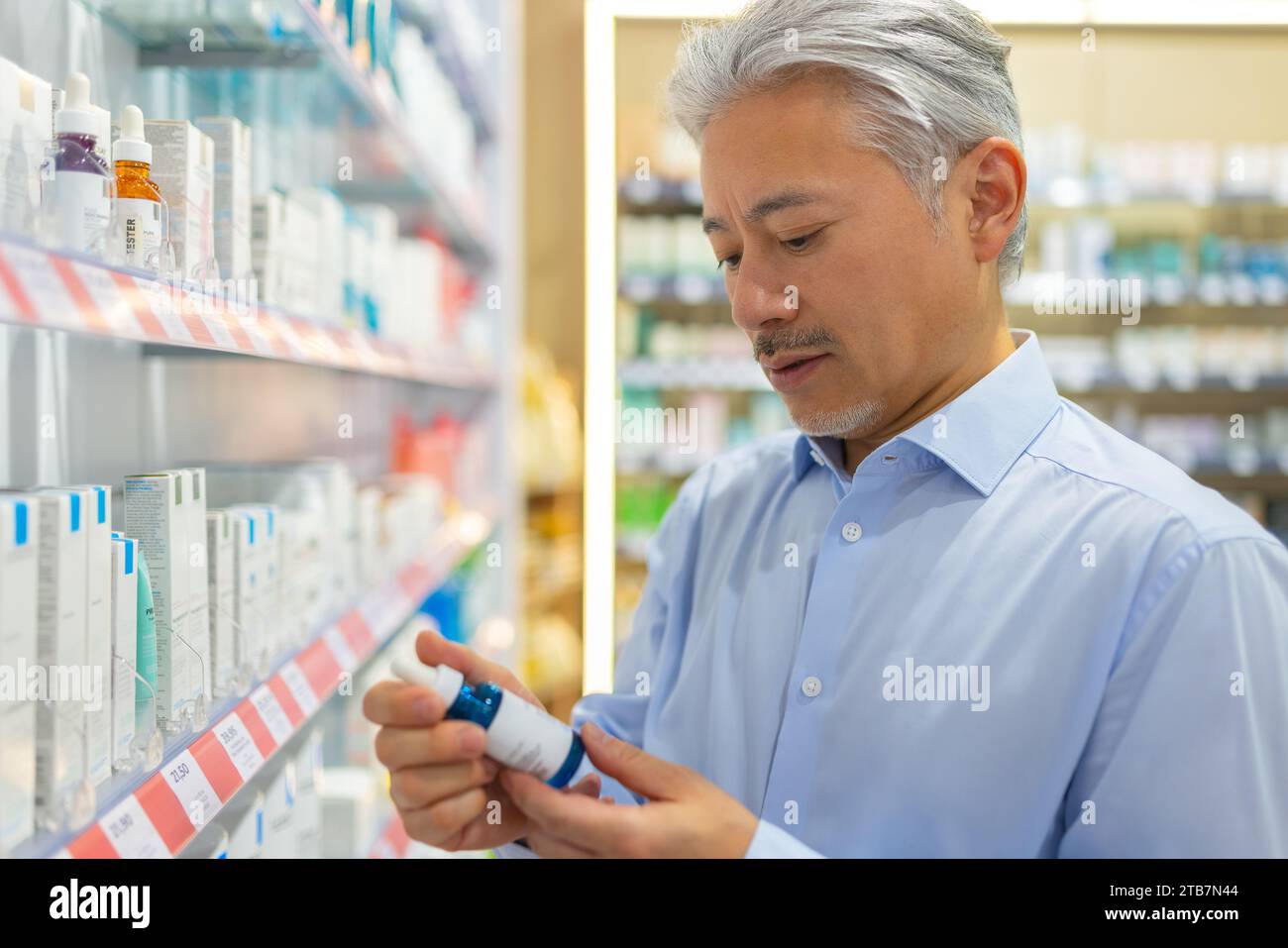 Leitender Mann, der das Produkt hält und Informationen überprüft, während er in einem pharmazeutischen Geschäft am Regal steht Stockfoto