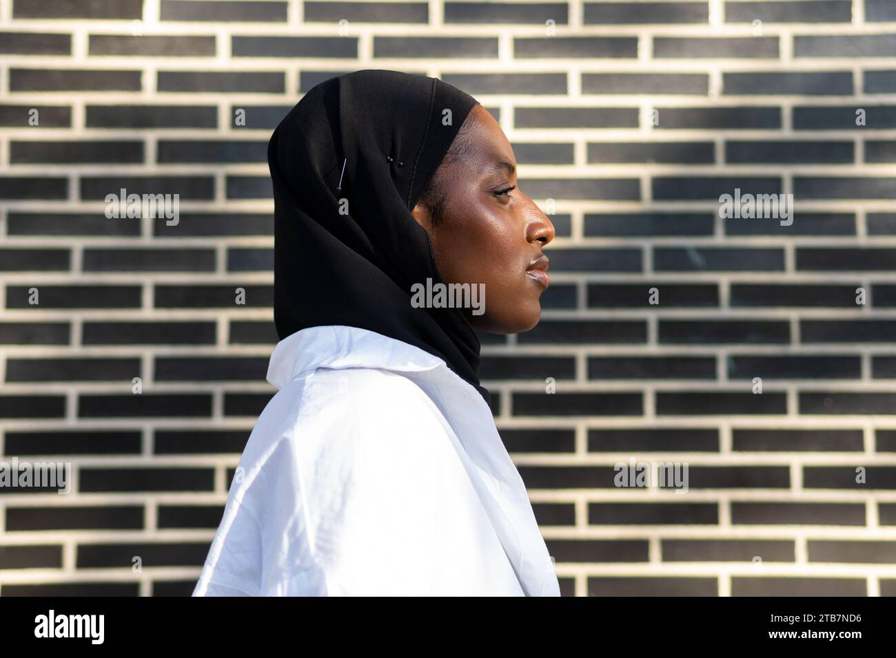 Porträt einer selbstbewussten afroamerikanischen muslimischen Unternehmerin in schwarzem Hijab und weißem formalen, die in der Stadt an einer Ziegelmauer steht Stockfoto