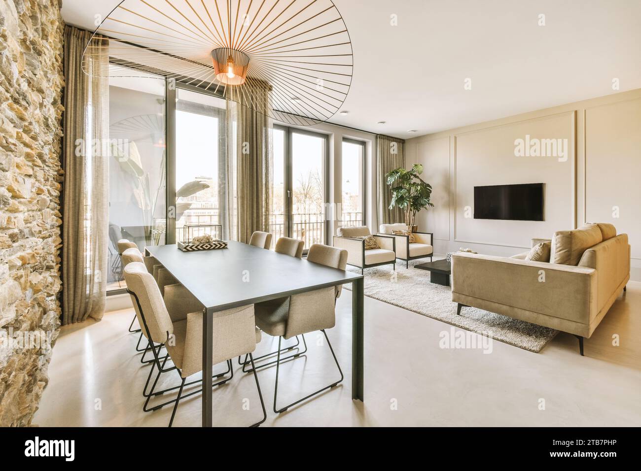 Esstisch mit Stühlen und Sofa vor dem Fernseher neben einem großen Fenster im geräumigen Wohnzimmer des modernen Apartments Stockfoto