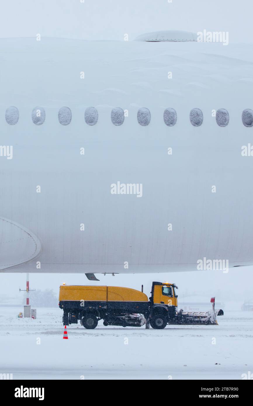 Winter frostiger Tag am Flughafen bei starkem Schneefall. Mit Schnee bedecktes Flugzeug gegen Schneepflüge, die die Start- und Landebahn des Flughafens räumen. Stockfoto