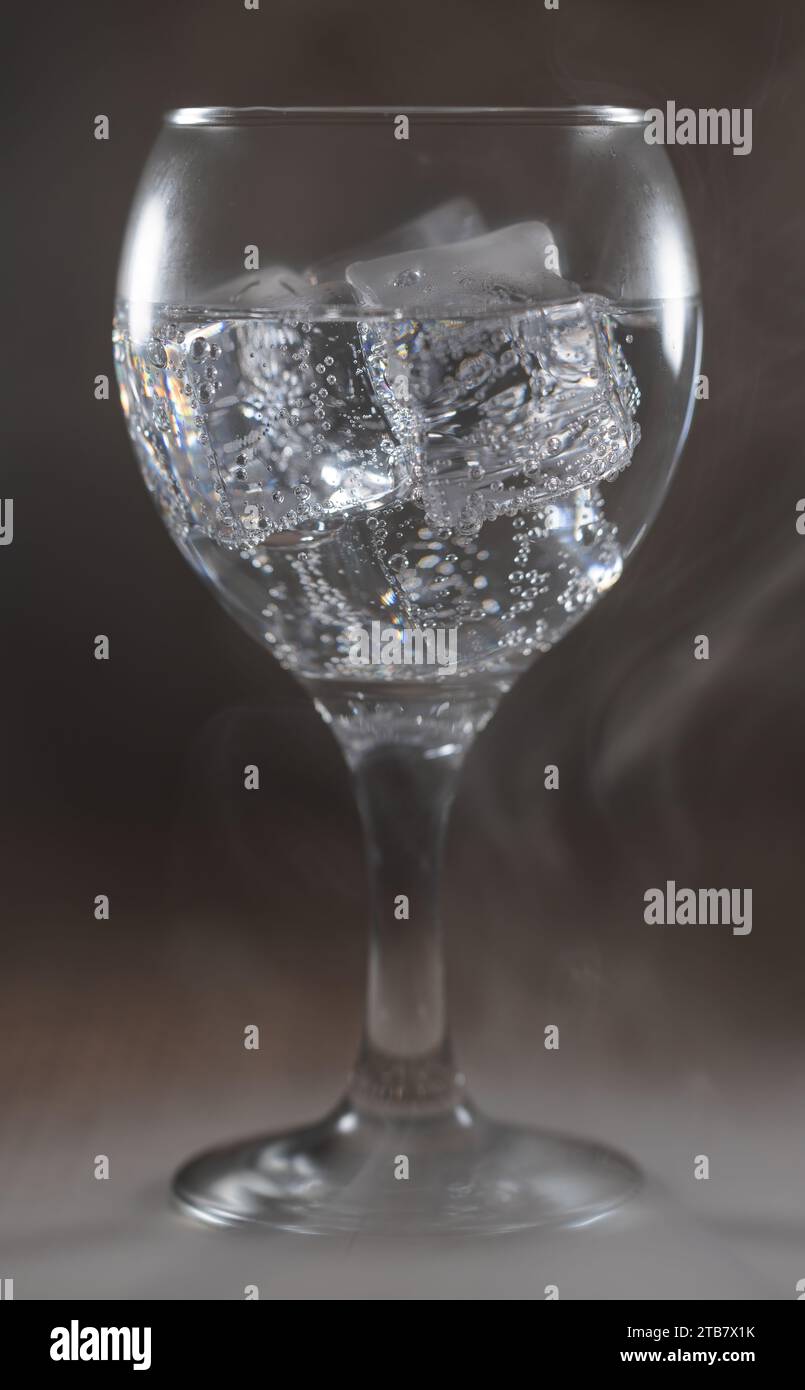 Ein Nahaufnahme-Bild einer Hand, die einen klaren Eiswürfel in ein Glas Wasser gießt Stockfoto