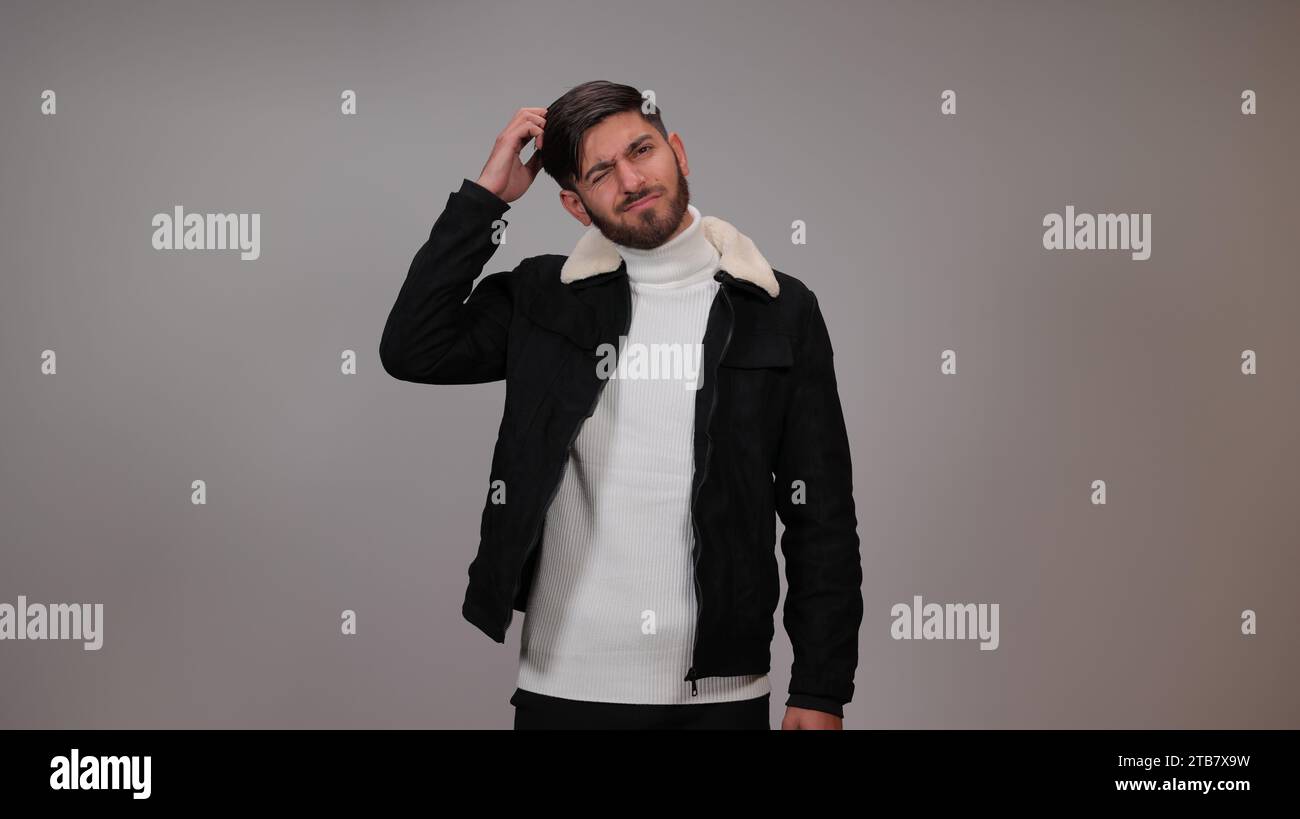 Ein verwirrter junger Mann, der vor grauem Hintergrund denkt. Stockfoto