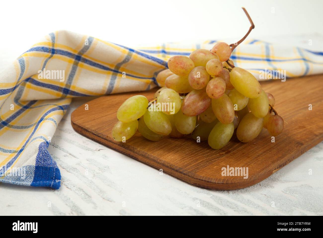 Schneidebrett mit einem großen Haufen reifer rosafarbener Trauben auf weiß. Rosafarbene Weintrauben mit blauem Küchentuch auf weißem hölzernem Hintergrund. Stockfoto