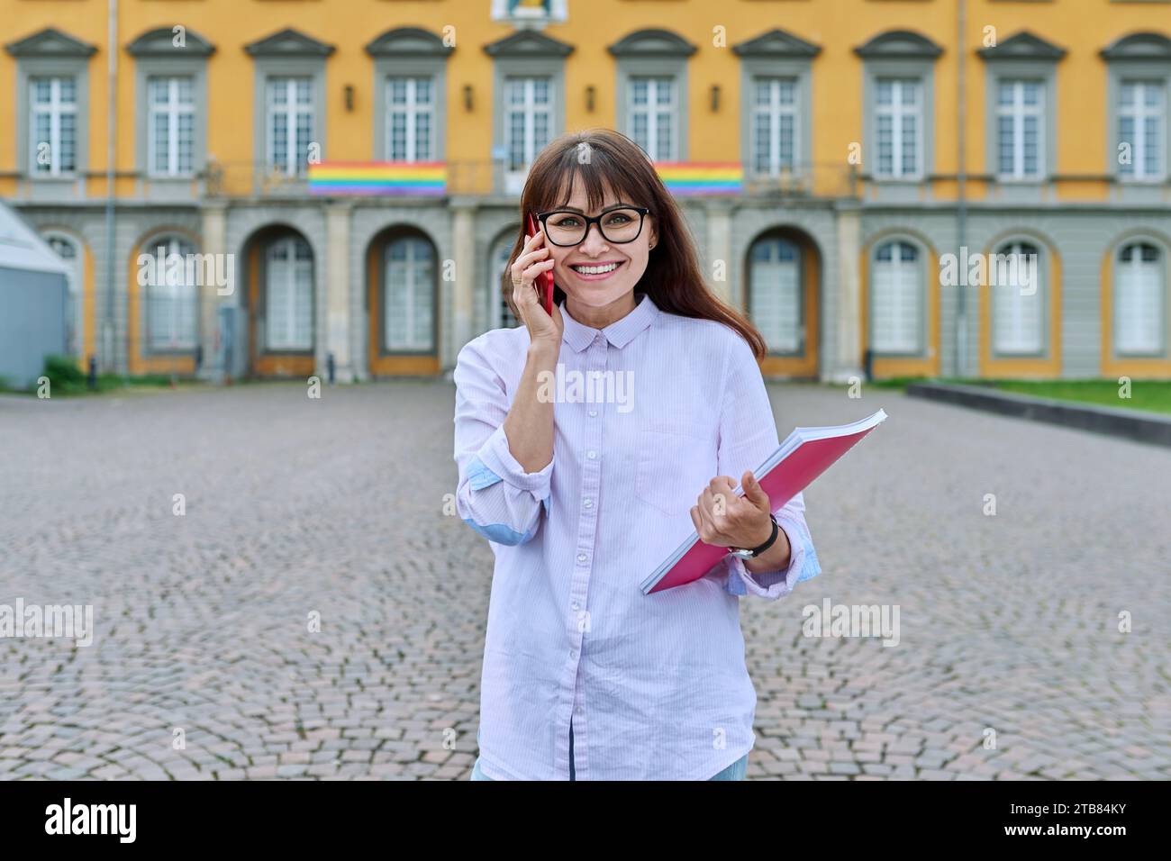 Lehrerin mittleren Alters mit Smartphone, Hintergrund des Bildungsgebäudes Stockfoto
