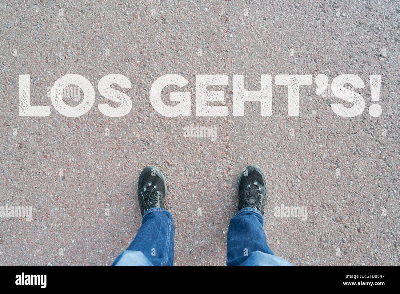 „Los geht's“ (los geht's) als deutsches Motivationszitat auf der Straße mit Schuhen daneben Stockfoto