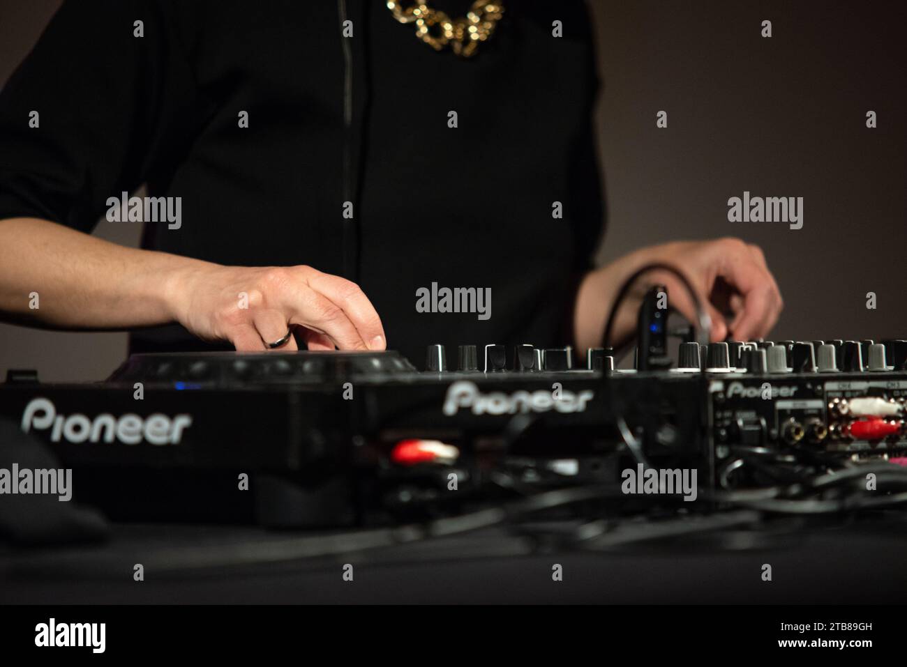 DJ (Disc Jockey) Party Set mit Pionneer Mischkonsole, schwarzem T-Shirt und großer Goldkette. Nahaufnahme der Hände Stockfoto