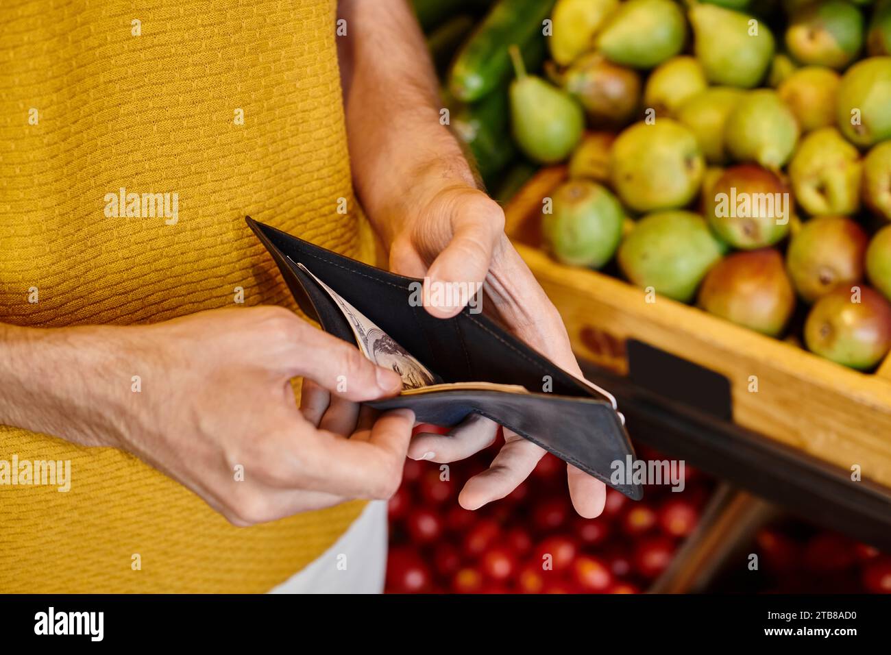 Zugeschnittene Ansicht eines reiferen männlichen Kunden, der seine Geldbörse in der Hand hält, um im Lebensmittelgeschäft zu bezahlen Stockfoto