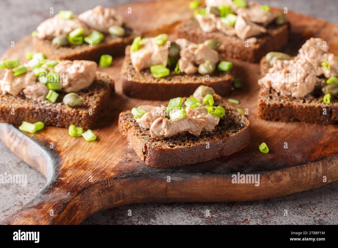 Leckere Sandwiches mit Kabeljauleber, Kapern und grünen Zwiebeln in Nahaufnahme auf einem Holzbrett auf dem Tisch. Horizontal Stockfoto