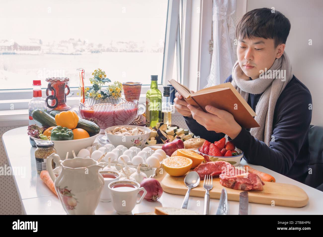Junger asiatischer Mann, der ein Buch liest und alleine am Esstisch speisen und im Winter an Thanksgiving Essen und Trinken feiern kann Stockfoto