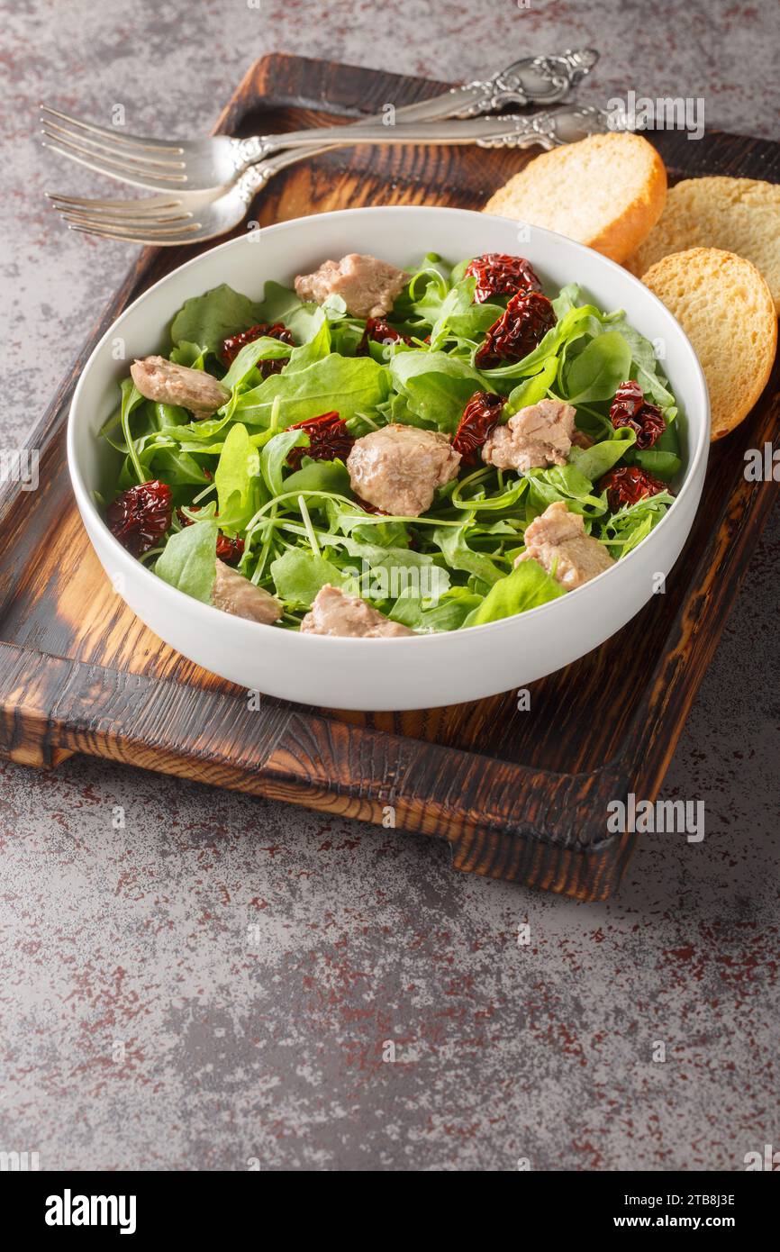 Gesundes Essen Kabeljau Lebersalat mit gemischtem Blattgemüse und sonnengetrockneten Tomaten in einer Schüssel auf dem Tisch. Vertikal Stockfoto