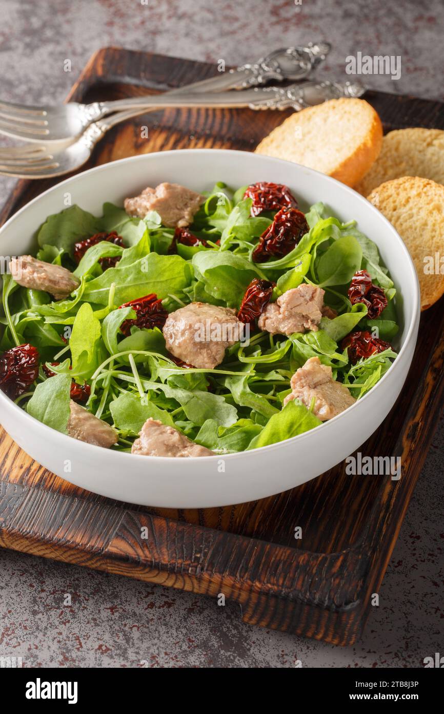Kabeljaulebersalat mit Rucola und sonnengetrockneten Tomaten in einer Schüssel auf dem Tisch. Vertikal Stockfoto