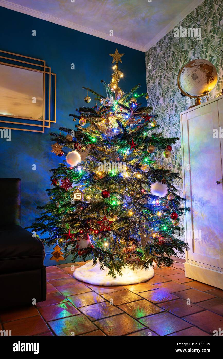 Wunderschöner weihnachtsbaum in einem gemütlichen Haus, dekoriert und beleuchtet von hellen Girlanden, die sich auf dem Boden spiegeln. Stockfoto