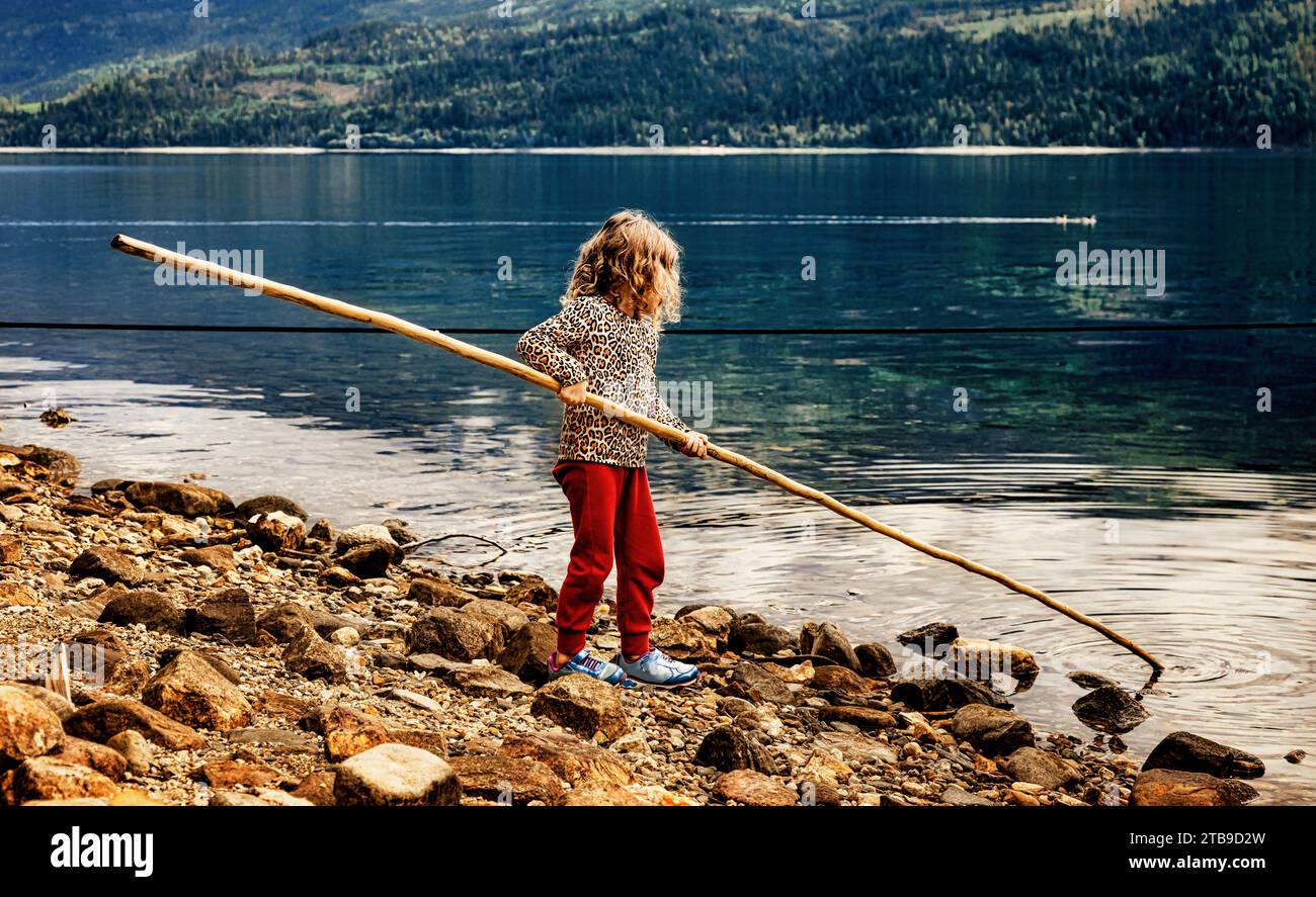 Ein junges Mädchen, das mit einer Stange an einer Küste des Shuswap Lake in British Columbia, Kanada spielt Stockfoto