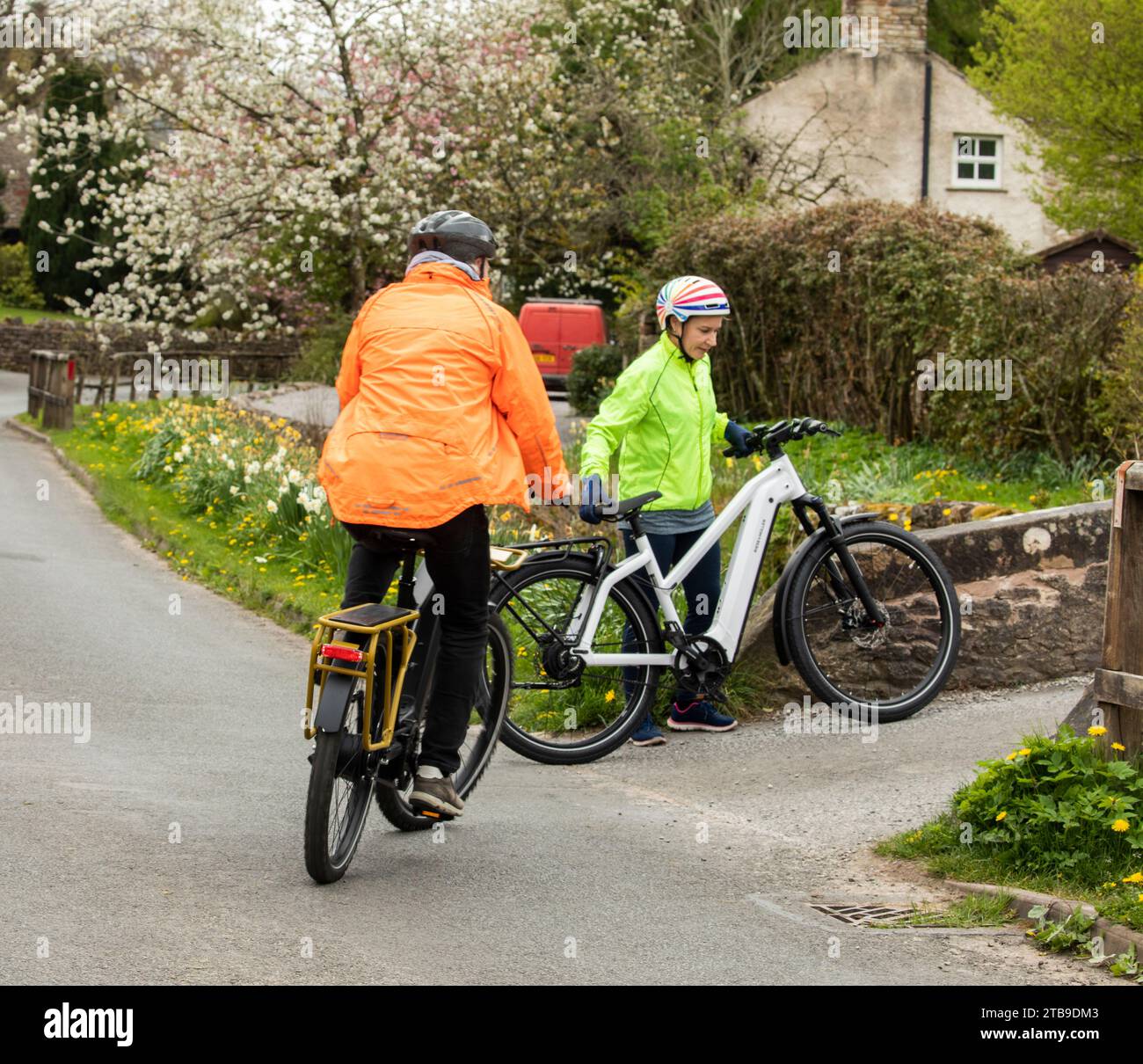 Mann und Frau Radfahrer fahren E-Bikes in einem hübschen Dorf im Frühling, Hartley. Kirkby Stephen, North Pennines, Cumbria Stockfoto