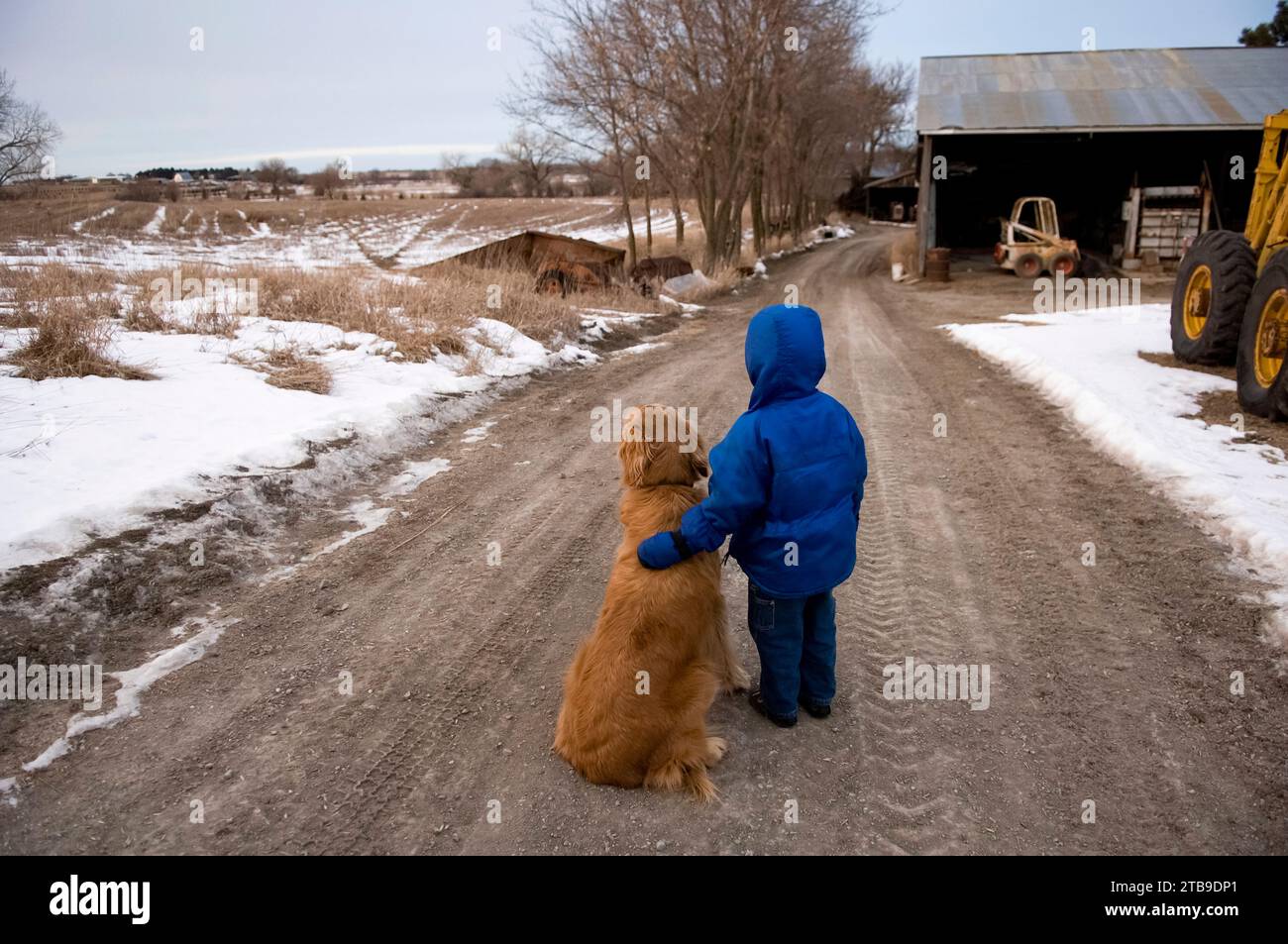 Junge steht auf einer Schotterstraße mit einem goldenen Retriever; Cortland, Nebraska, Vereinigte Staaten von Amerika Stockfoto