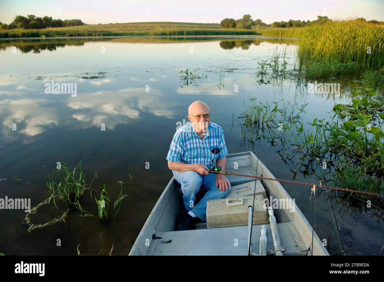 Senior man sitzt in einem Ruderboot und geht in einem Teich nach Largemouth Bass fischen; Bennet, Nebraska, Vereinigte Staaten von Amerika Stockfoto