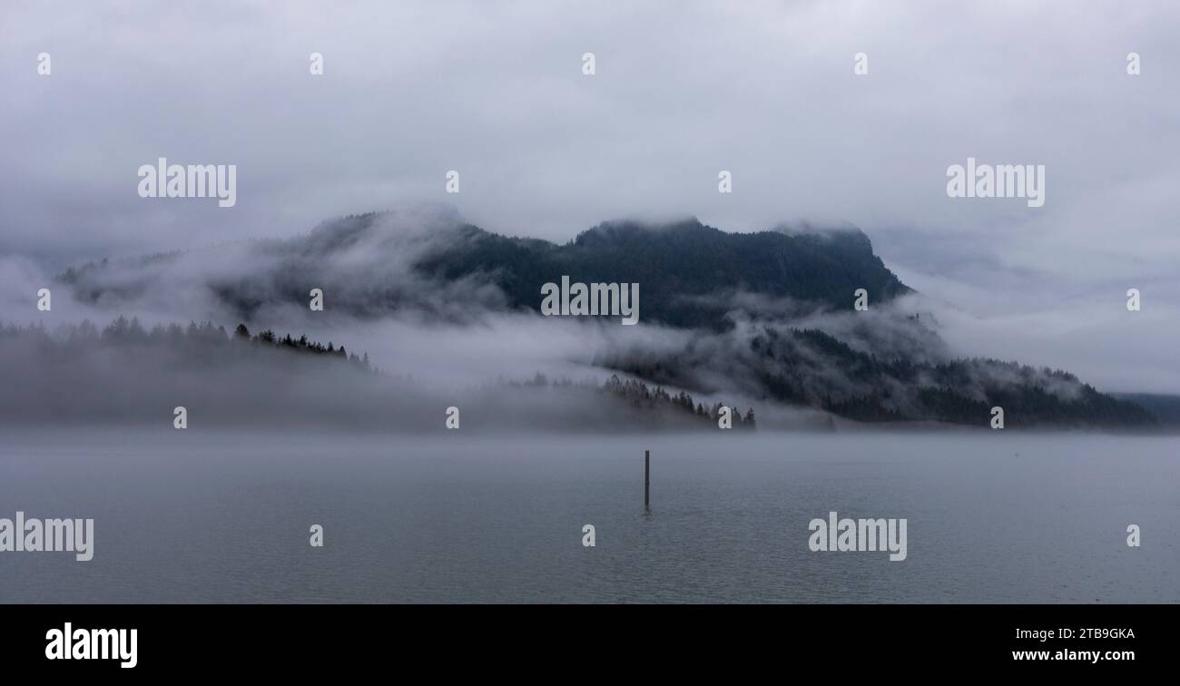 Atemberaubender Blick vom Spaziergang entlang des Deiches am Pitt Lake in Maple Ridge auf einen Berggipfel, der an einem grauen Tag von Nebel bedeckt ist Stockfoto