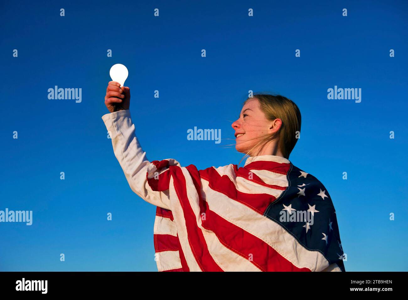 Die Glühbirne leuchtet in der Hand eines Mädchens, das in eine amerikanische Flagge gehüllt ist; Lincoln, Nebraska, Vereinigte Staaten von Amerika Stockfoto