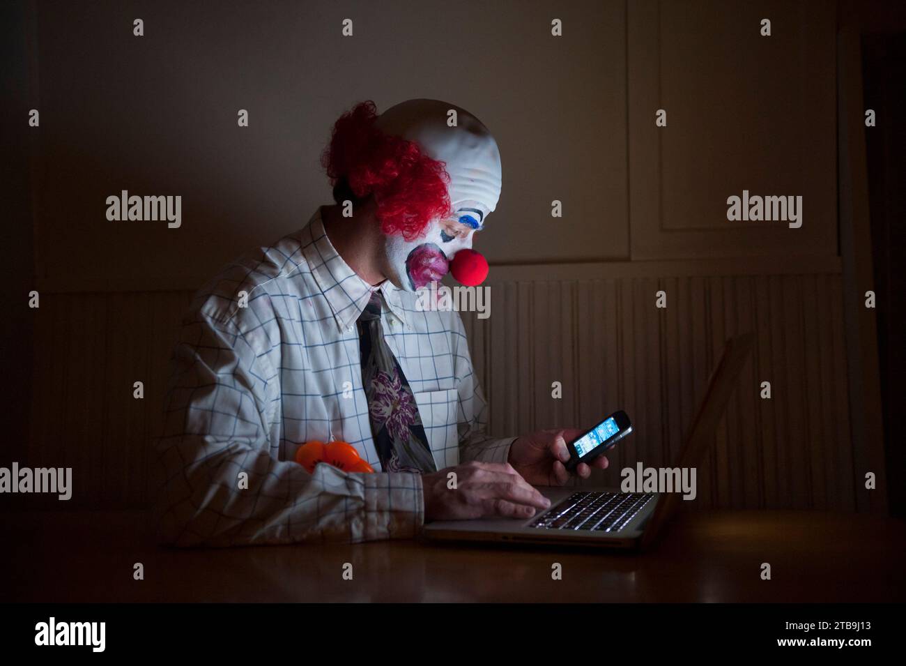 Clown mit Hemd und Krawatte benutzt gleichzeitig einen Laptop und ein Smartphone; Lincoln, Nebraska, Vereinigte Staaten von Amerika Stockfoto