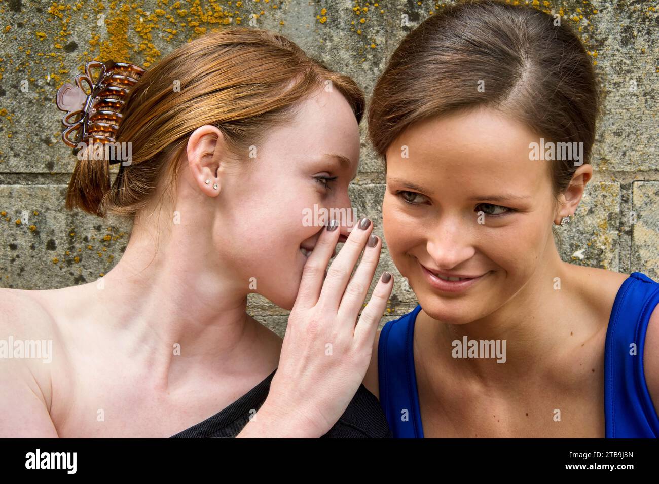 Zwei junge Frauen in Formalwear flüstern einander Geheimnisse zu; Lincoln, Nebraska, Vereinigte Staaten von Amerika Stockfoto