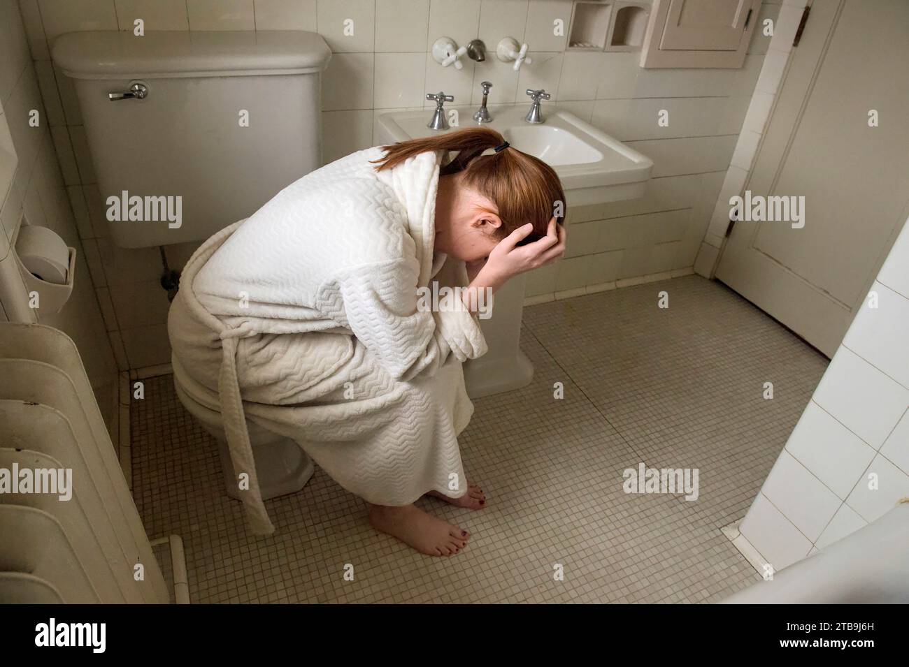 Eine junge Frau in einem Bademantel sitzt unbequem in ihrem Badezimmer; Lincoln, Nebraska, USA Stockfoto