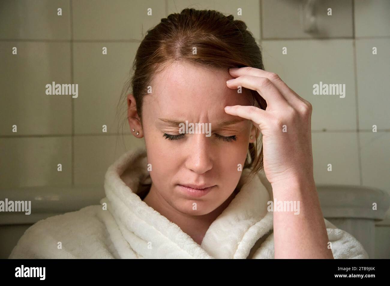 Eine junge Frau in einem Bademantel sitzt unbequem in ihrem Badezimmer; Lincoln, Nebraska, USA Stockfoto