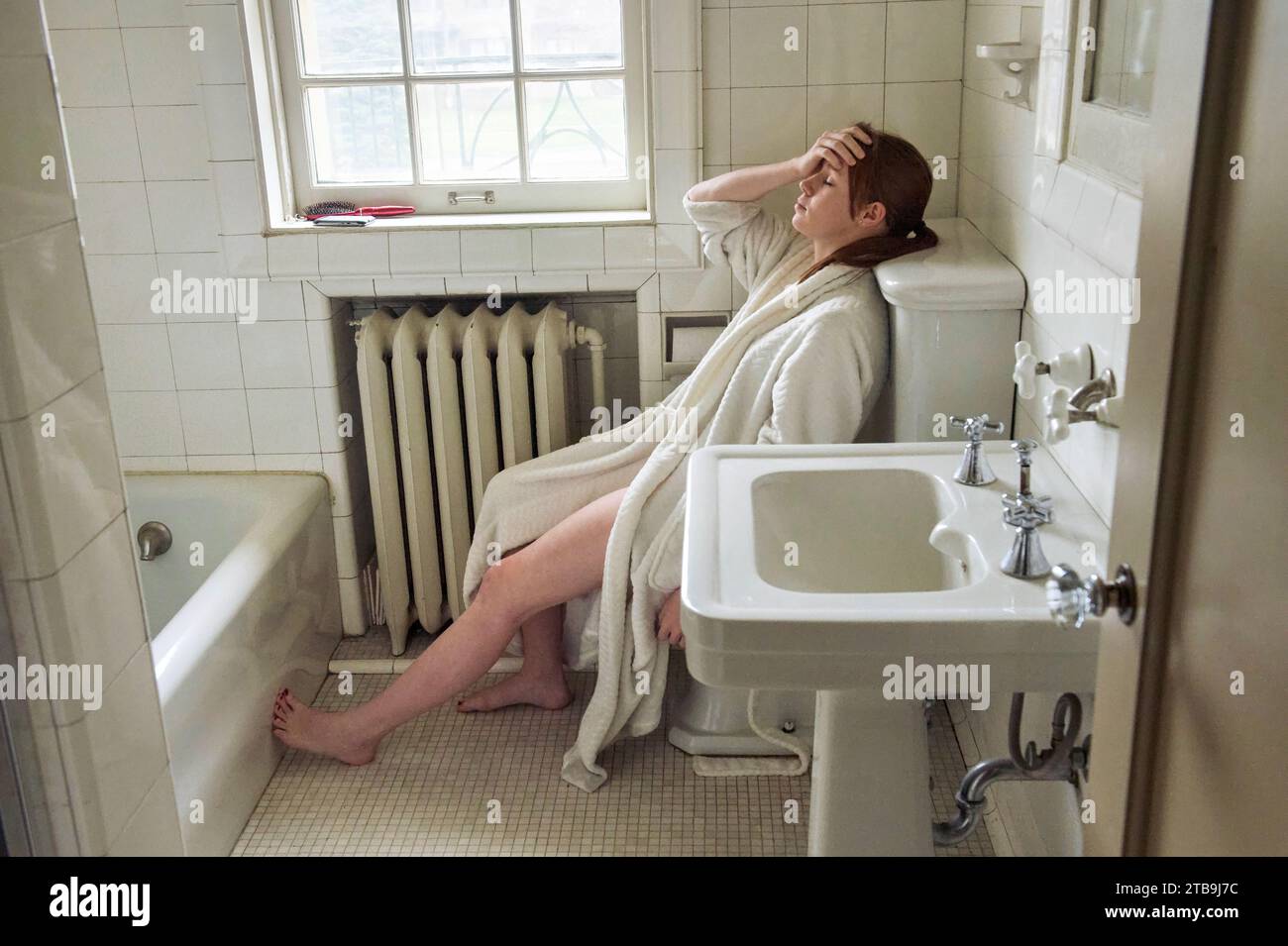 Eine junge Frau sitzt mit dem Kopf in ihrem Badezimmer; Lincoln, Nebraska, USA Stockfoto