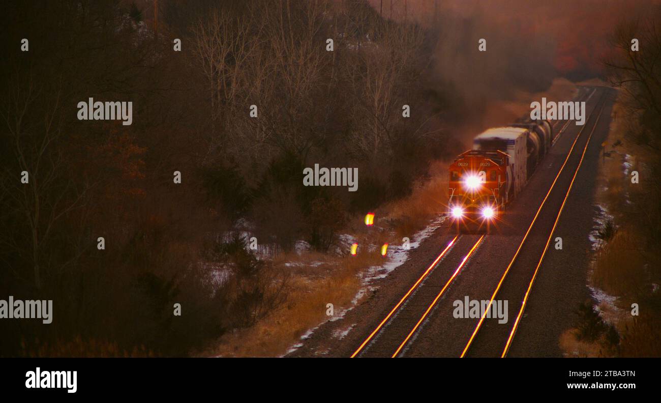 Kurzer Güterzug, der zur magischen Stunde durch den waldreichen ländlichen mittleren westen fährt, mit Herbstlaub. Stockfoto