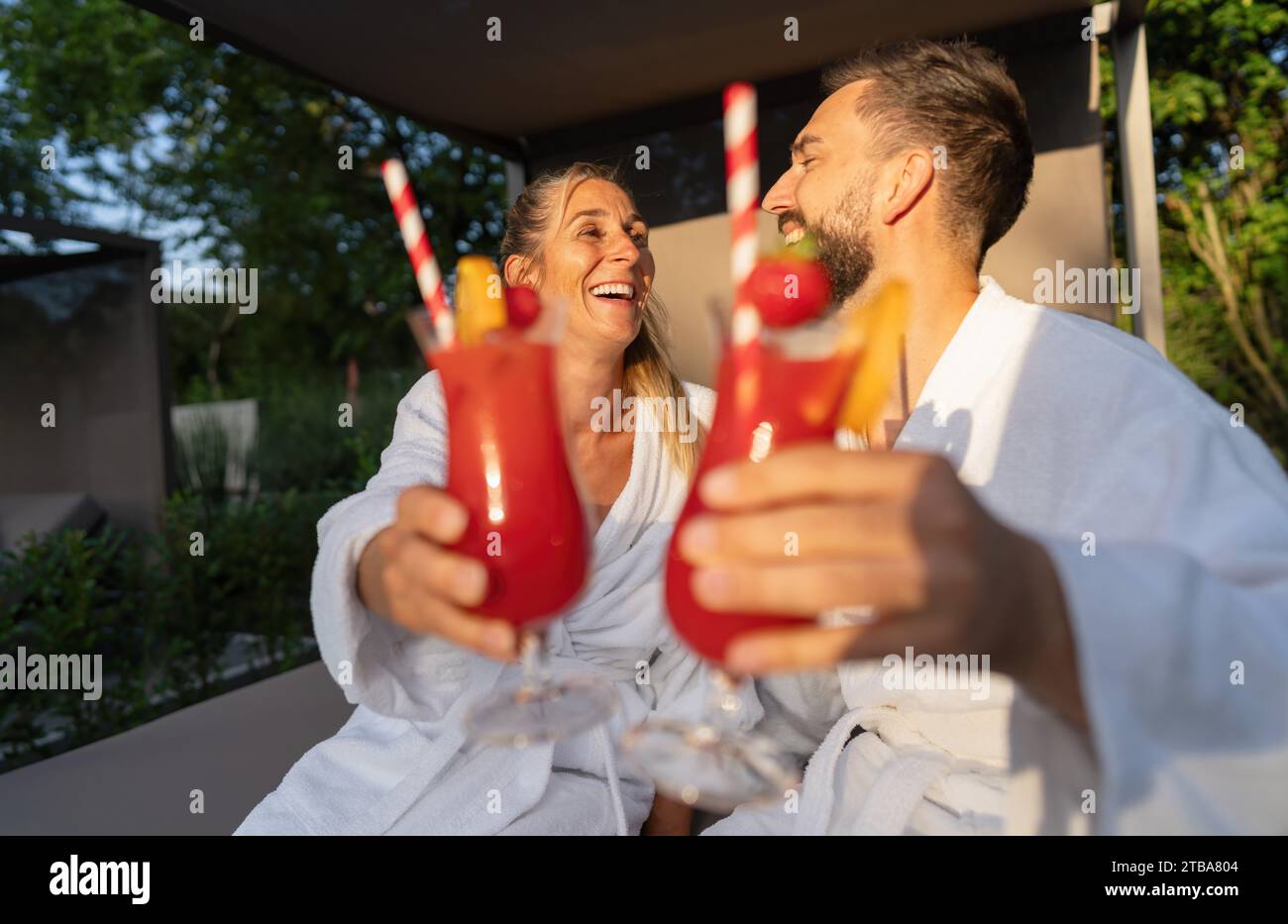 Paare in weißen Bademänteln, die draußen im Spa Resort mit roten Cocktails locken Stockfoto