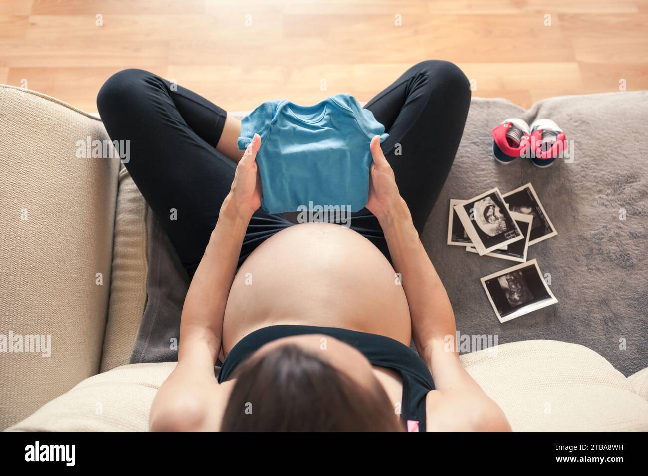 Schwangere Mutter, die Babykleidung hält und sich auf ein neues Familienmitglied vorbereitet Stockfoto