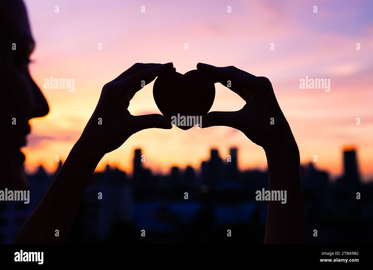 Hand hält Herz auf einem Hintergrund des Sonnenuntergangs der Stadt Stockfoto