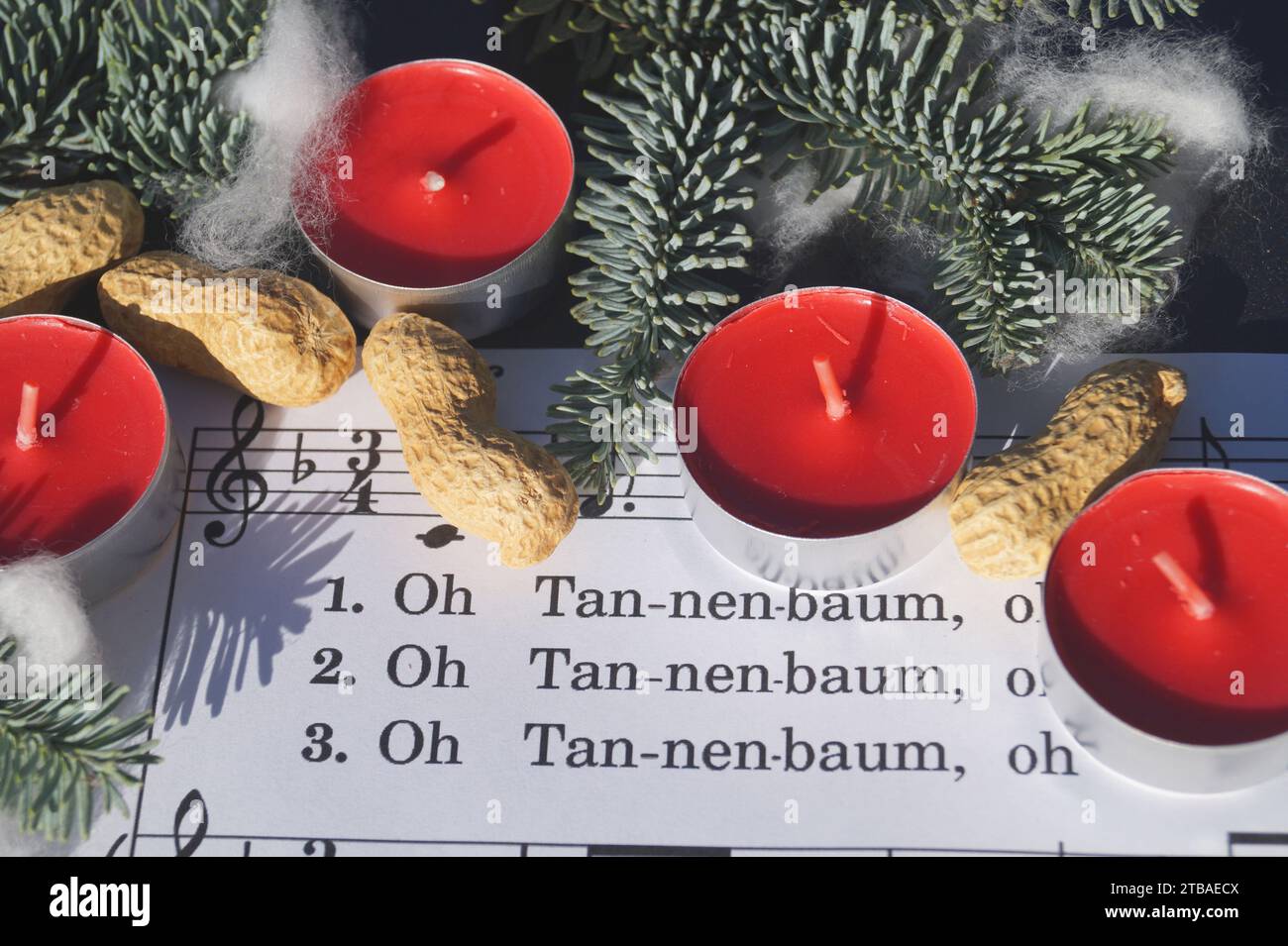 Notenblatt mit dem Weihnachtslied „Oh Tannenbaum“, dekoriert mit Teelichtern, Erdnüssen und Tannenzweigen Stockfoto