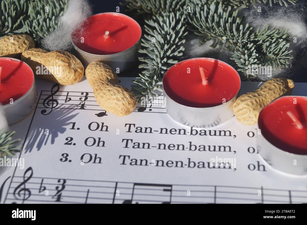 Notenblatt mit dem Weihnachtslied „Oh Tannenbaum“, dekoriert mit Teelichtern, Erdnüssen und Tannenzweigen Stockfoto