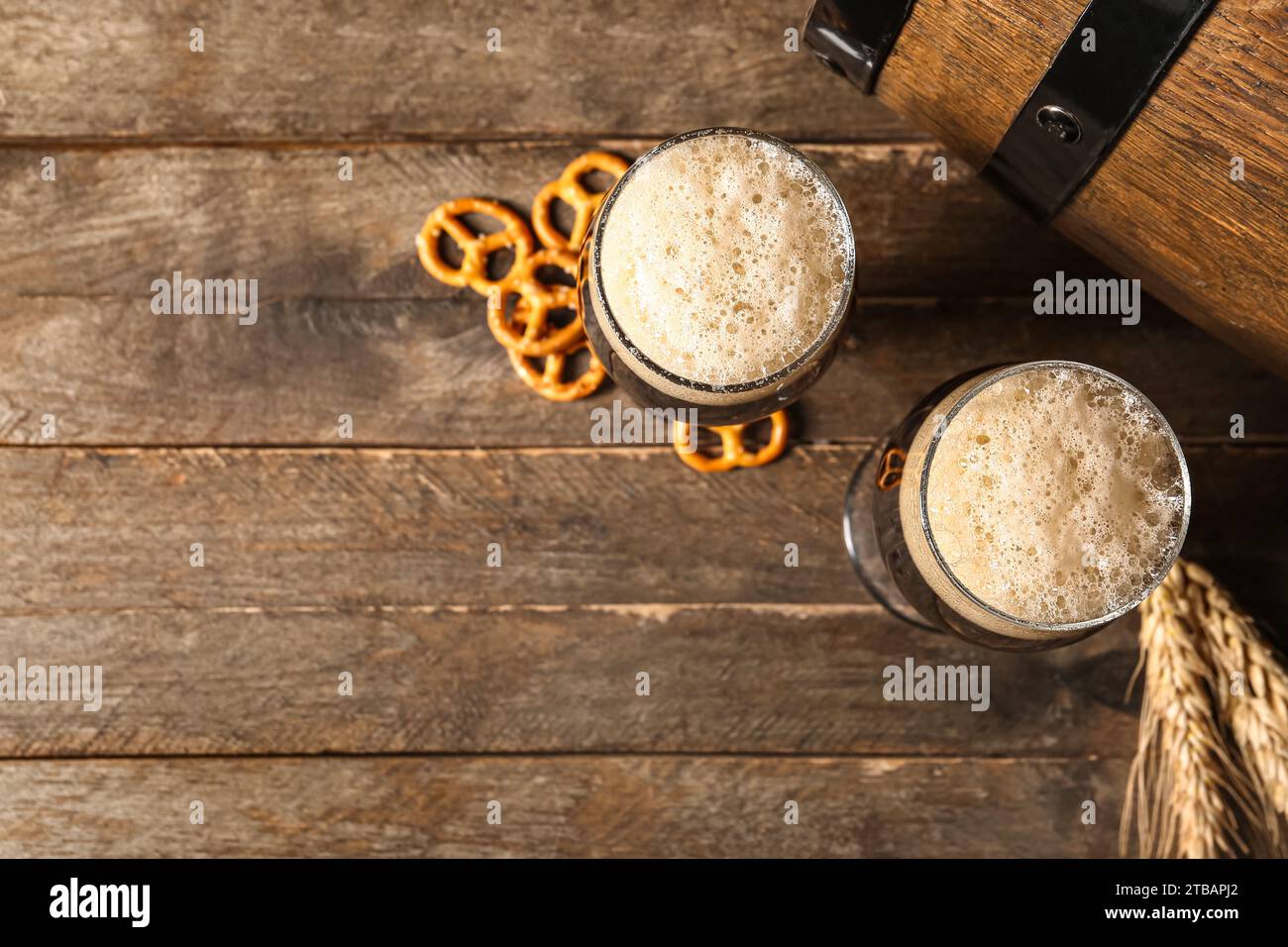 Gläser und Fass mit kaltem dunklem Bier mit Weizen und Brezeln auf hölzernem Hintergrund Stockfoto