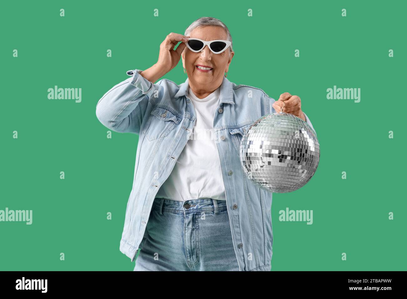 Ältere Frau mit Discoball auf grünem Hintergrund Stockfoto