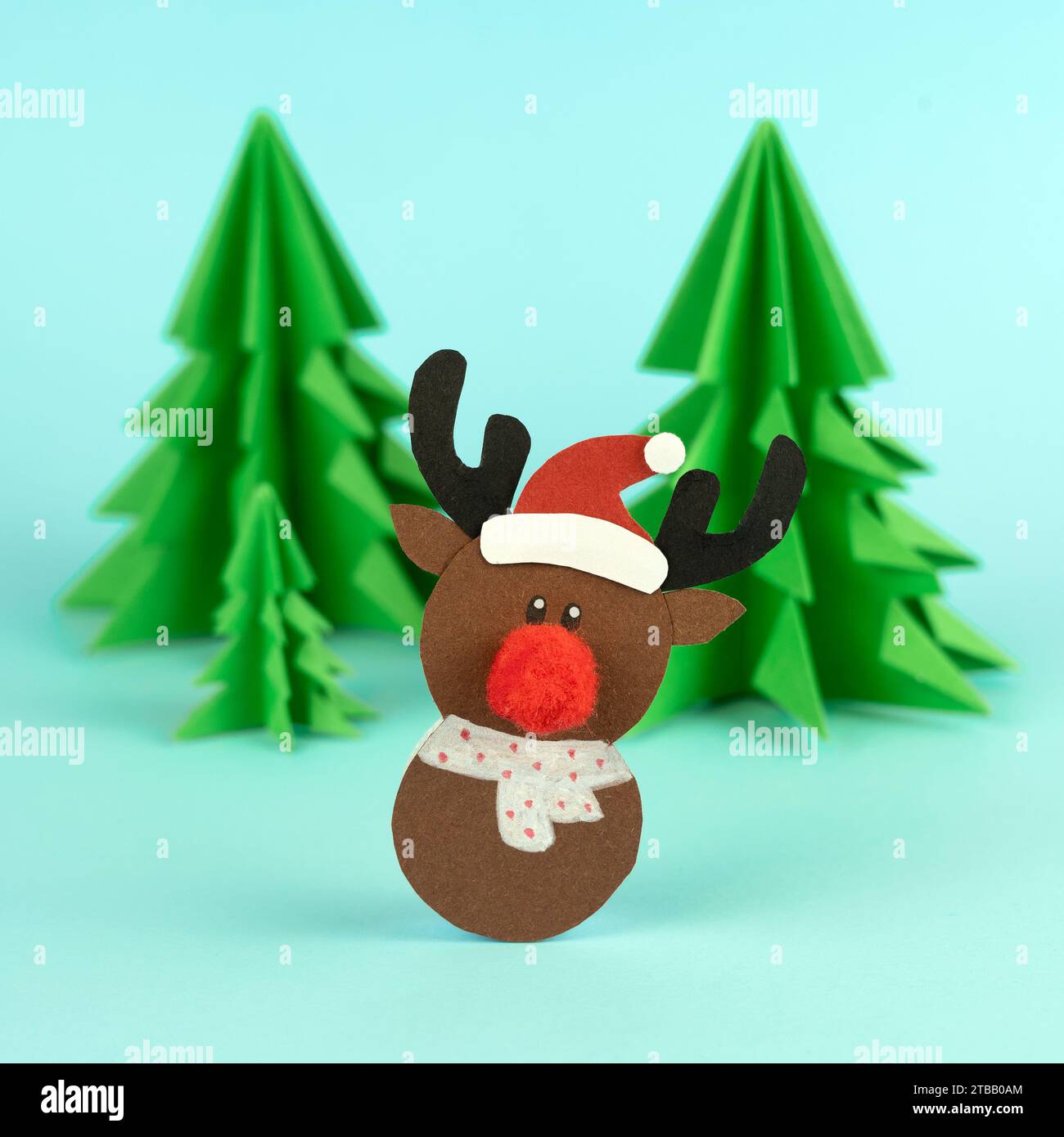 Handgemachte süße Rentiere mit Tannen aus Papier auf blauem Hintergrund Stockfoto