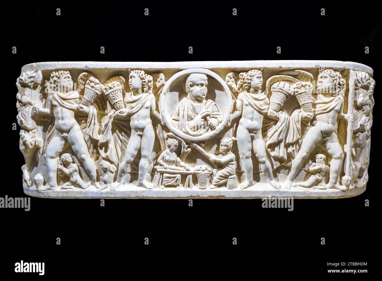 Tub-Sarkophag mit Darstellung nur auf der Vorderseite und gewölbten Seiten. Ein zentraler Kreis (Clipeus), der den Verstorbenen mit einer Schriftrolle in der linken Hand darstellt, wird von zwei geflügelten männlichen Figuren gestützt, die, gepaart mit ähnlichen anderen, als Personifizierungen der vier Jahreszeiten interpretiert, Körbe voller reichlicher und verschiedener Früchte halten. In der Mitte unter dem Klypeus, Schauplatz des täglichen Lebens. Weißer Marmor 3. Jahrhundert n. Chr. - Cattedrale di San Gerlando (Kathedrale von Agrigento) - Sizilien, Italien Stockfoto