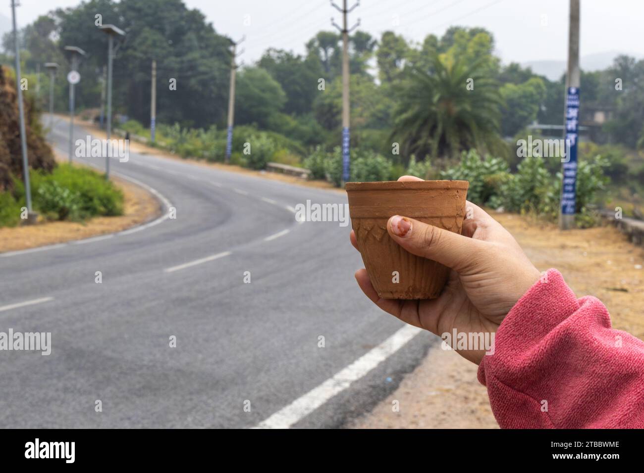Ein Mädchen genießt heißen Tee, serviert in einer traditionellen Töpfertontasse mit verschwommener Autobahnlandschaft Stockfoto